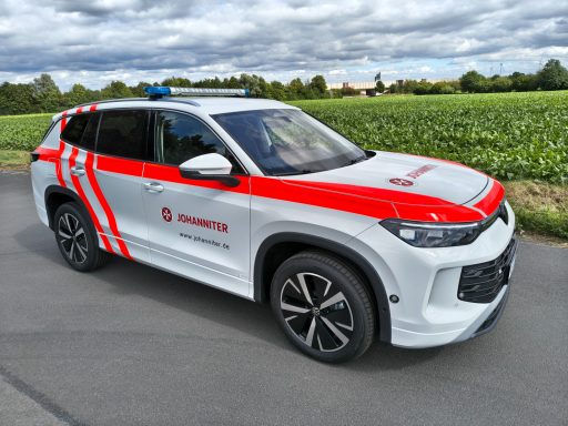 Prototyp VW Tayron Rotes und weißes Einsatzfahrzeug mit blauen Sirenen auf einer Straße zwischen Feldern.